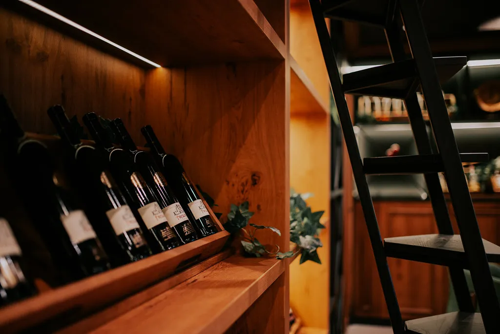 Naturvinflasker på trehyller ved baren, med en stige inntil veggen.